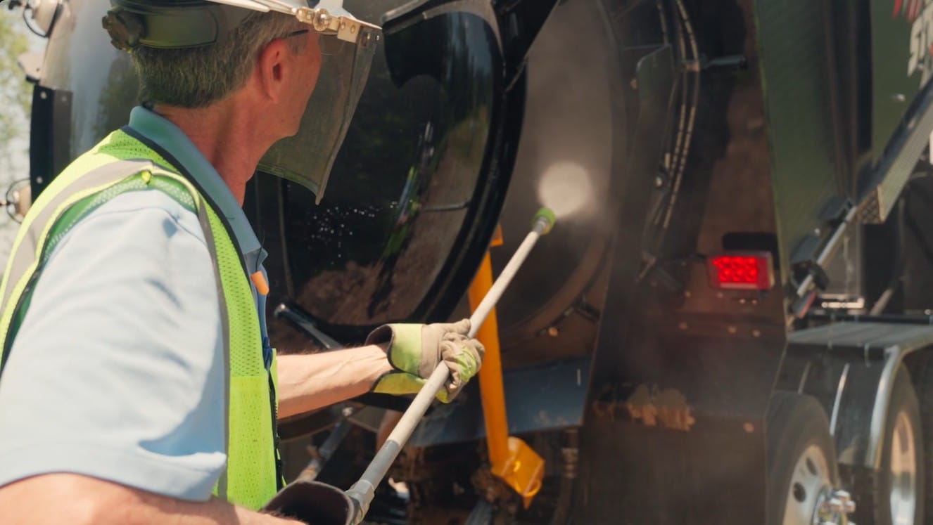 Worker in safety vest and face shield jetting water into an X-Vac hydro excavation truck tank.