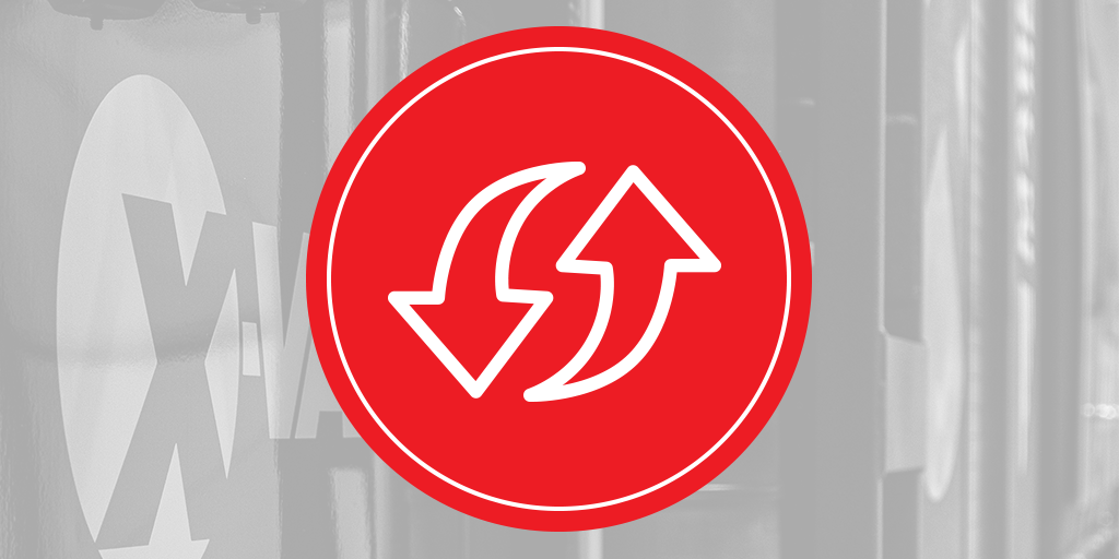 Red circular icon with opposing curved arrows overlaying a grayscale X‑Vac hydro excavation tank, symbolizing vacuum system flow.