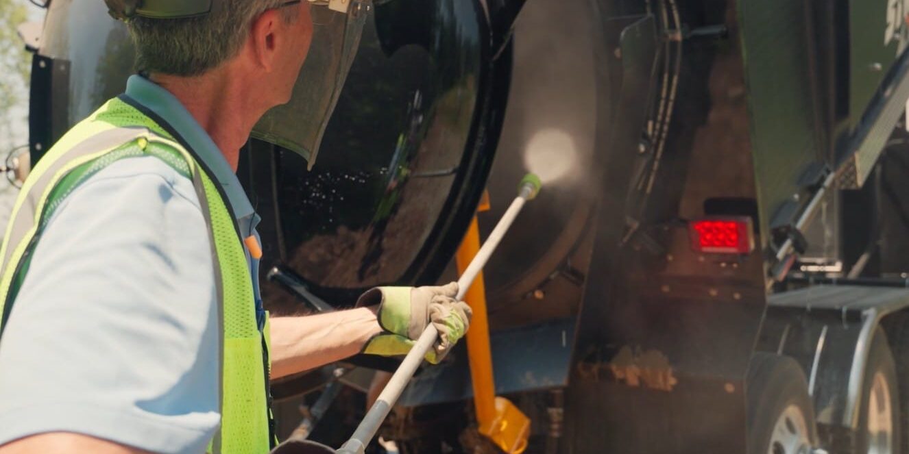 Worker in safety vest and face shield jetting water into an X-Vac hydro excavation truck tank.